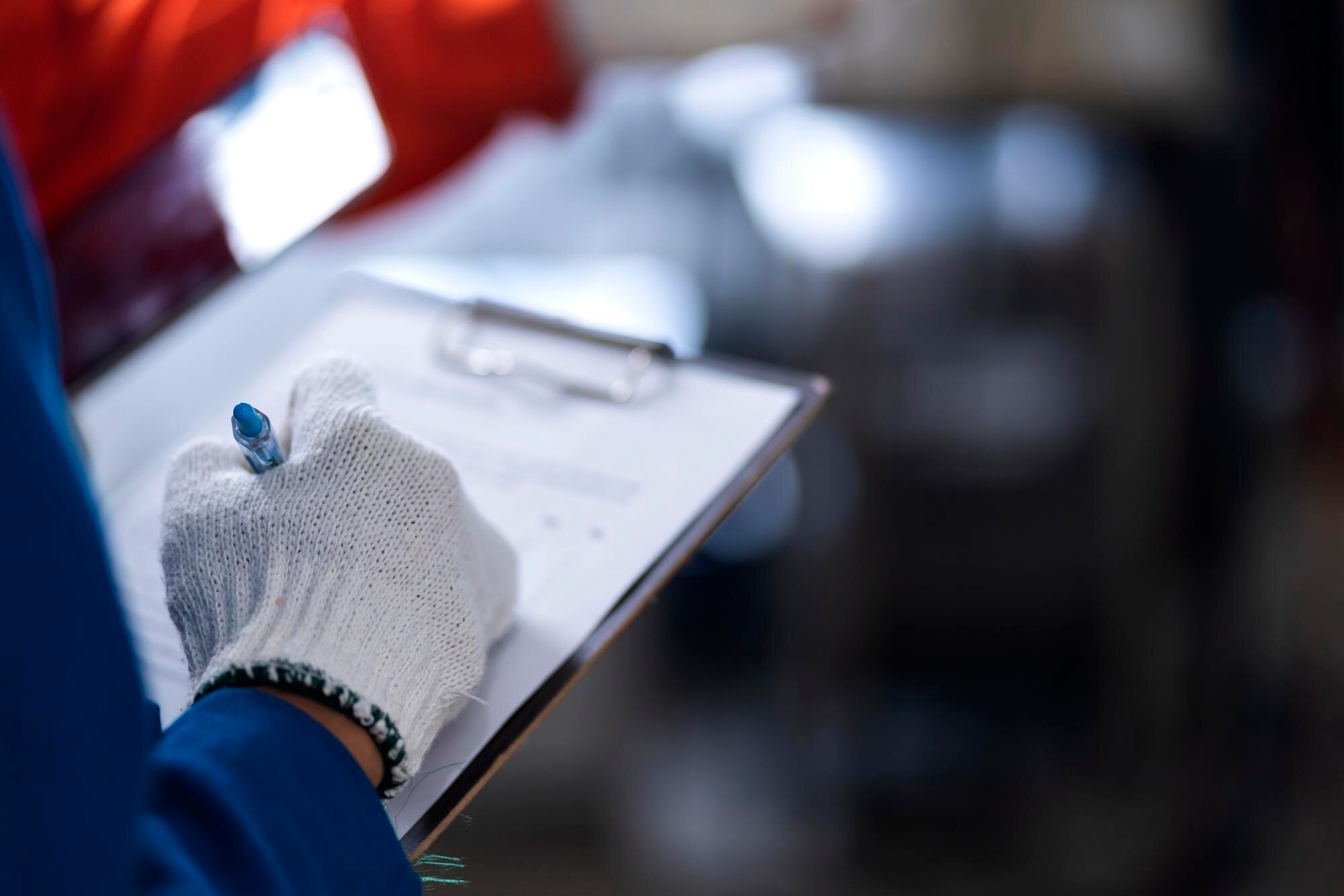 Profissional com luvas avaliando documentos em uma prancheta, representando o controle de qualidade e as certificações em fundição de precisão que garantem conformidade e desempenho industrial.