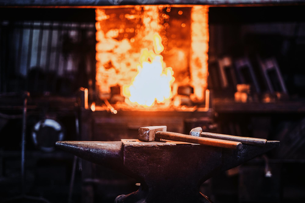 Forja industrial com bigorna e ferramentas aquecidas, ilustrando o uso de ligas metálicas na fundição de precisão em processos de conformação e fabricação de peças.
