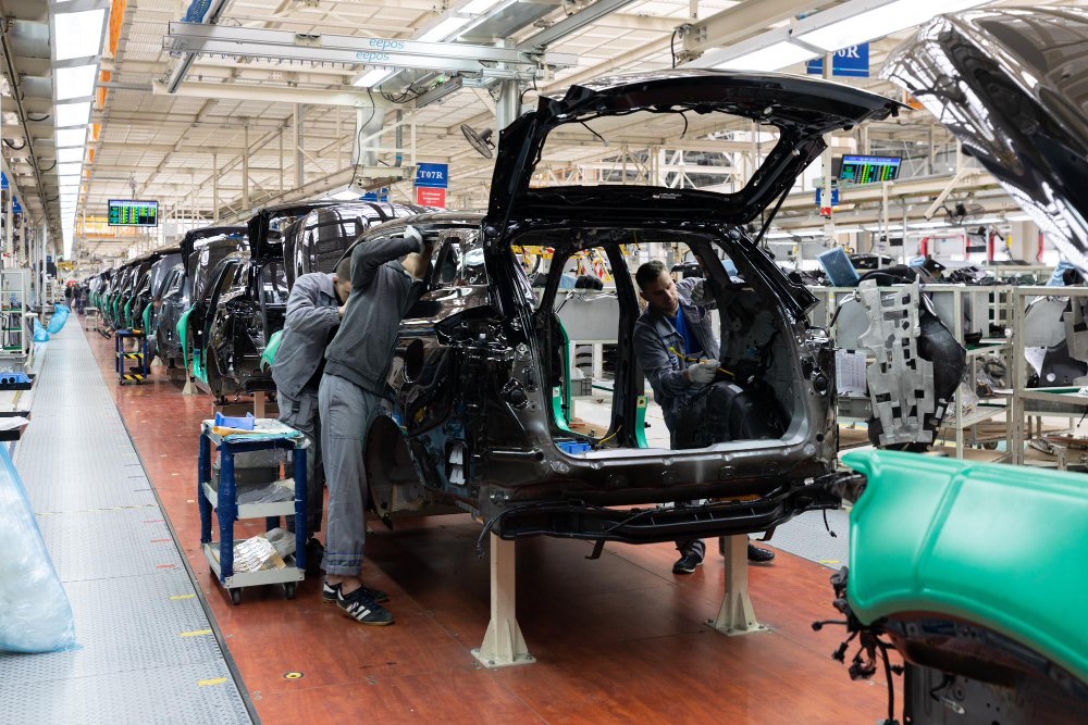 Linha de montagem automotiva com veículos em produção e técnicos realizando ajustes, representando exigências de qualidade alinhadas à IATF 16949 no setor automotivo.